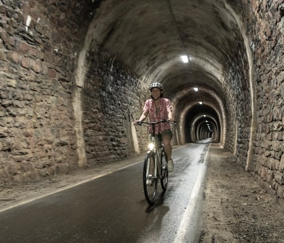 Eine Person fährt mit einem Fahrrad durch einen langen, beleuchteten Tunnel mit gemauerten Steinwänden., © Eifel Tourismus GmbH, D. Ketz Eine Person fährt mit einem Fahrrad durch einen langen, beleuchteten Tunnel mit gemauerten Steinwänden., © Eifel Tourismus GmbH, D. Ketz