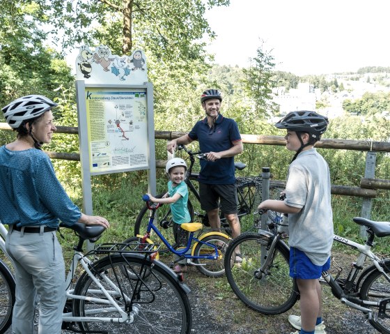 Familie mit Fahrrädern am Maare-Mosel-Radweg. Sie stehen vor einem Wegweiser, umgeben von grüner Landschaft. Alle tragen Fahrradhelme., © Rheinland-Pfalz Tourismus GmbH, D. Ketz Familie mit Fahrrädern am Maare-Mosel-Radweg. Sie stehen vor einem Wegweiser, umgeben von grüner Landschaft. Alle tragen Fahrradhelme., © Rheinland-Pfalz Tourismus GmbH, D. Ketz