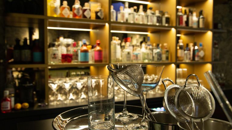 A stylish bar with a selection of spirits in the background. On a serving tray, cocktail glasses and bar strainer are ready.