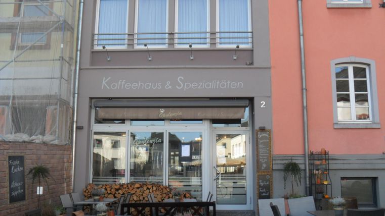Ein gemütliches Café mit Tischen im Außenbereich. Über der Tür steht "Kaffehaus & Spezialitäten".