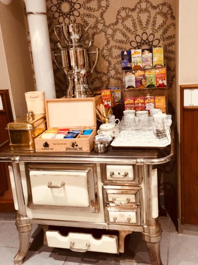 Ein dekorativer Tisch mit Teekanne, Teekästen und einer Auszeichnung steht vor einer gemusterten Wand. Der Tisch hat mehrere Schubladen und wirkt elegant.