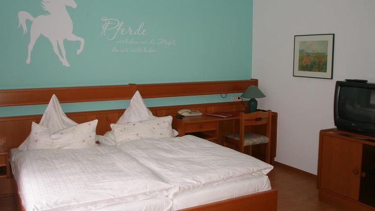 Ein gemütliches Schlafzimmer mit einem Doppelbett und zwei Kopfkissen. An der Wand befindet sich ein Pferdemotiv und der Raum ist in sanften Farben gehalten.