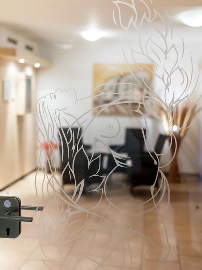 Eine dekorative Glastür mit floralen Mustern im Hintergrund. Im Inneren sind Essbereiche und moderne Möbel zu sehen.