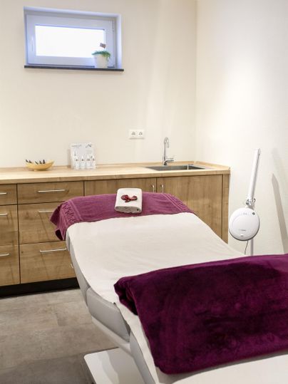 Ein gemütlicher Behandlungsraum mit einem Liegestuhl und Holzregalen. Die Farbgestaltung ist hell und einladend.