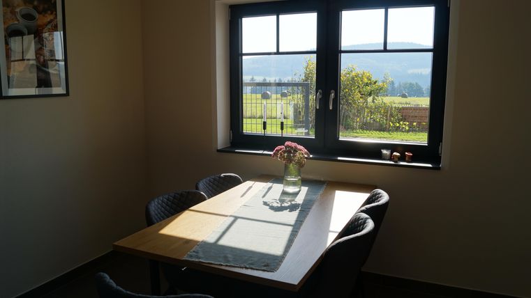 Ein gemütlicher Essbereich mit einem Holzstisch und Stühlen. Große Fenster bieten einen Blick ins grüne Freie.