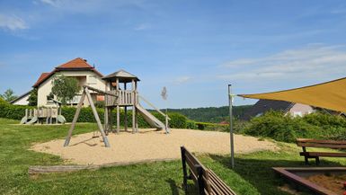 Sandspielplatz mit Holz-Kinderspieltürmen und großem Sandkasten mit Sonnensegel.