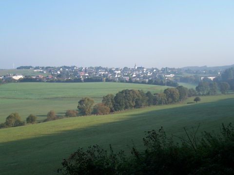 Eine ruhige Landschaft mit sanften Hügeln und einem kleinen Dorf in der Ferne. Der Himmel ist klar und es ist eine friedliche Atmosphäre.