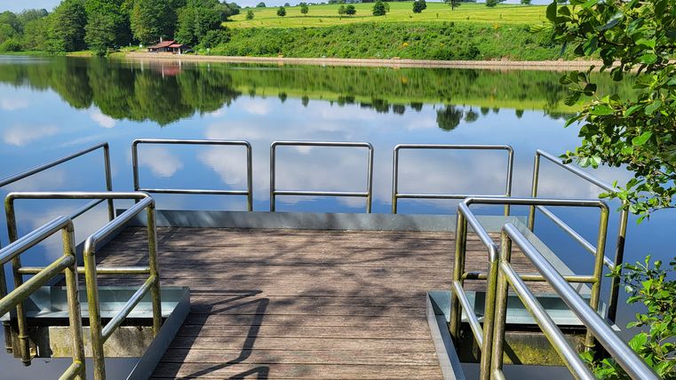 Der Blick auf einen Steg am Stausee und die weitere grüne Landschaft