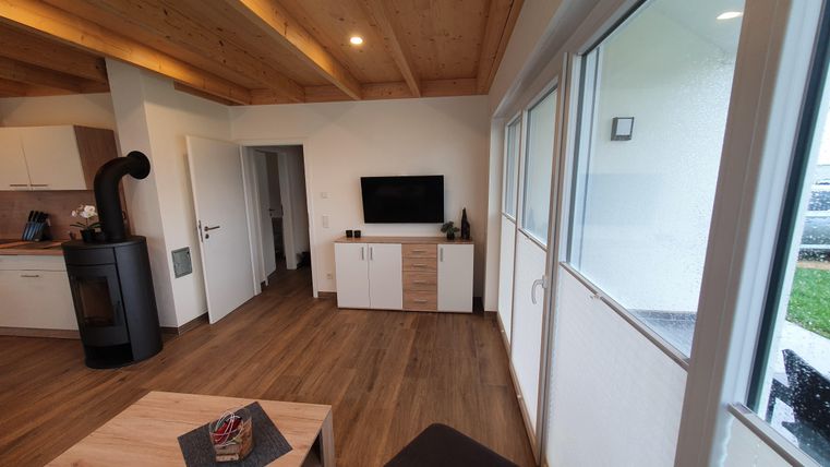 Ein modernes Wohnambiente mit Holzdecke und warmem Licht. Der Raum enthält einen Fernseher, einen Tisch und einen gemütlichen Sessel.