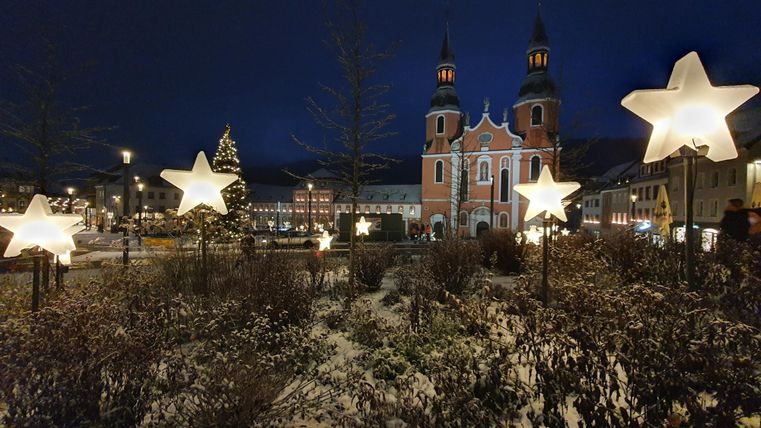 Eine beeindruckende Kirche mit zwei hohen Türmen liegt vor einem malerischen Hintergrund. Umgeben von historischen Gebäuden und Bäumen erstreckt sich ein großzügiger Platz.