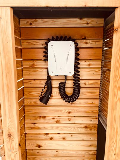 Eine Telefonzelle mit einer weißen Telefonanlage an einer Holzwand. Der Telefonhörer hängt an einer schwarzen Spiralschnur.