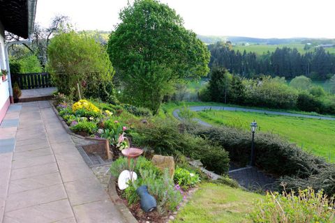 Eine schöne Gartenlandschaft mit bunten Blumen und einem gepflasterten Gehweg. Im Hintergrund sind grüne Hügel und Bäume zu sehen.
