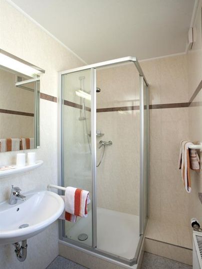 Ein modernes Badezimmer mit einer Duschkabine und einem Waschbecken. Die Wände sind hell und schlicht, mit Handtüchern und Pflegeprodukten dekoriert.