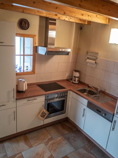 Eine moderne Küche mit Holzdecke und hellen Schränken. Der Raum ist gut ausgestattet mit Herd, Spüle und Fenstern für natürliches Licht.