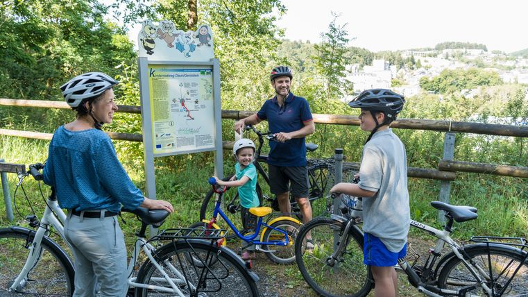 Familie mit Fahrrädern steht an einem Wegweiser auf dem Maare-Mosel-Radweg.