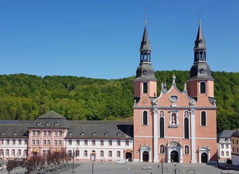 Eine beeindruckende Kirche mit zwei Türmen und einer roten Fassade. Im Hintergrund sind grüne Hügel zu sehen.