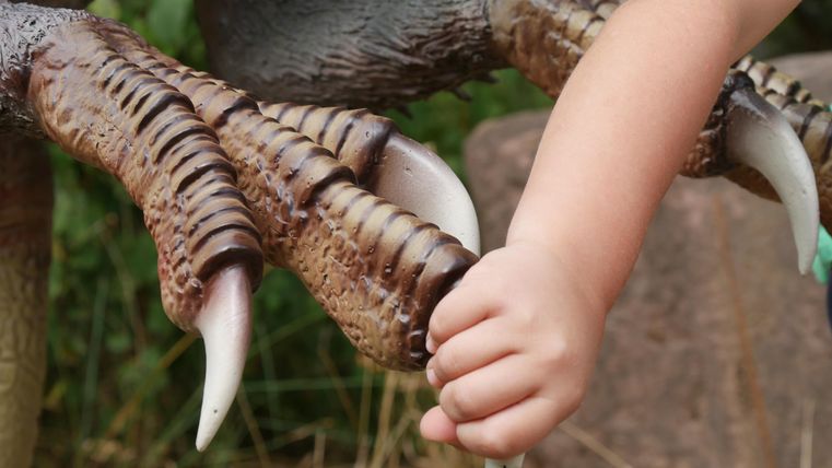 Un enfant tient les griffes d'un modèle de dinosaure. La scène montre une interaction entre l'enfant et la sculpture.