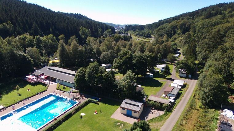 Ein schöner Campingplatz mit einem Schwimmbad und viel grünem Raum. Im Hintergrund sind Wälder und Hügel zu sehen.