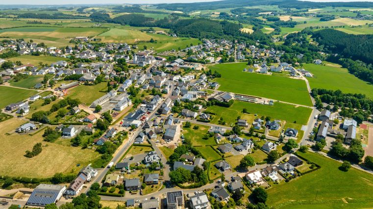 Eine malerische Landschaft mit einem kleinen Dorf und vielen Häusern. Die Umgebung ist grün und hügelig, ideal für ländliche Idylle.