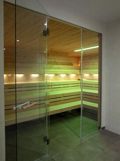 Eine moderne Sauna mit Glasschiebetüren und warmem Holzinterieur. Sanfte Beleuchtung schafft eine entspannende Atmosphäre.