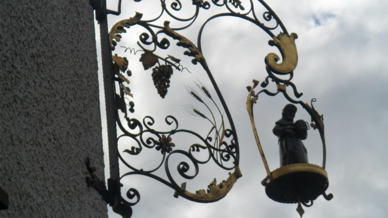 Eine kunstvolle eiserne Schaukel mit goldenen Verzierungen und einer Statue. Im Hintergrund sind Wolken zu sehen.