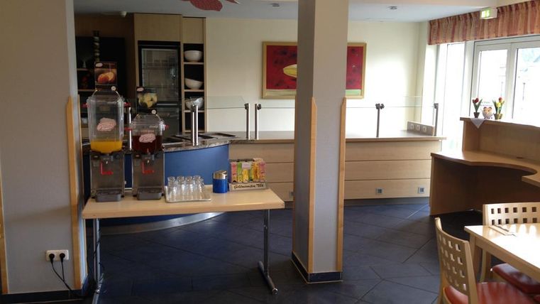 Ein moderner Cafébereich mit einem Getränkeautomaten und Tischen. Helle Wände und große Fenster sorgen für eine einladende Atmosphäre.