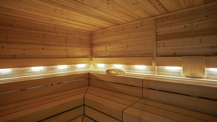 Eine moderne Sauna mit Holzverkleidung und sanfter Beleuchtung. Der Raum strahlt Wärme und Entspannung aus.