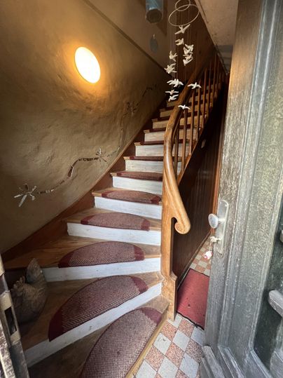 Ein einladender Treppenaufgang mit Holzgeländer. Die Stufen sind mit Teppichen in sanften Farben geschmückt, und ein rundes Fenster sorgt für natürliches Licht.