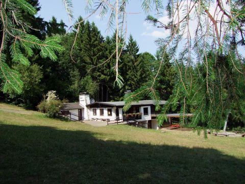 Ein ruhiges Haus in einer grünen Umgebung mit Bäumen im Hintergrund. Die sonnige Atmosphäre vermittelt ein Gefühl von Entspannung und Naturverbundenheit.