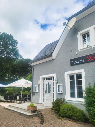 Ein charmantes Restaurant mit dem Namen "Pizzeria Lino". Draußen gibt es Sitzplätze und Sonnenschirme in einem angenehmen Garten.
