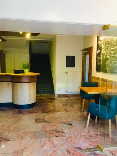 Ein einladender Empfangsbereich mit einem modernen Empfangstresen und einem Tisch. Im Hintergrund sind Treppen zu sehen, die zu weiteren Bereichen führen.