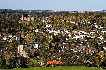 Eine malerische Stadt mit traditionellen Häusern und einem Blick auf eine alte Burg. Die umliegenden Wälder zeigen herbstliche Farben.
