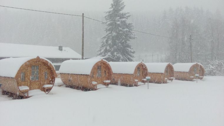 Holzhütten im Schnee mit starkem Schneefall umgeben. Die Landschaft ist winterlich und ruhig.