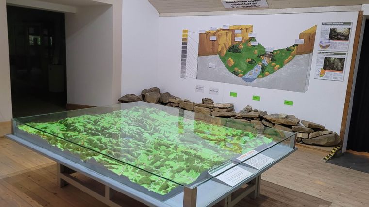 An interactive map on a table displays a green terrain. In the background, there is a wall map with additional information.