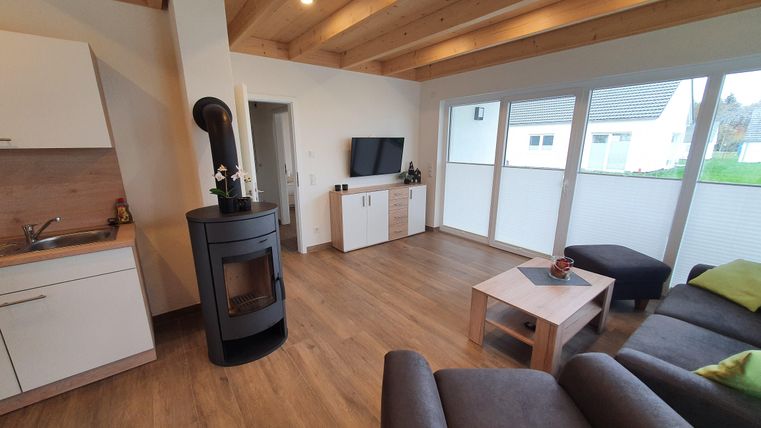 Modernes Wohnzimmer mit Holzdecken und großen Fenstern. Eine gemütliche Sitzecke und ein Kamin schaffen eine einladende Atmosphäre.