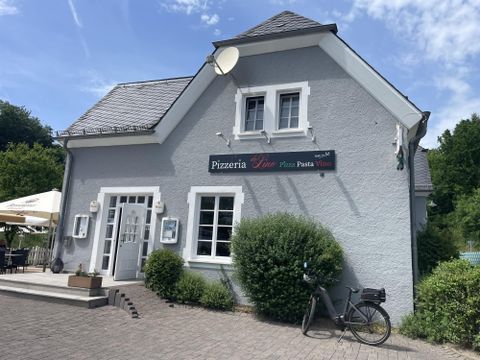 A cozy pizza restaurant with a gray facade and an inviting entrance area. In front of the building stands a bicycle and some plants.