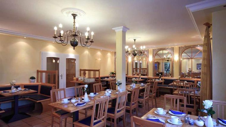 Ein einladender Speisesaal mit Holzmöbeln und eleganten Kronleuchtern. Die Tische sind liebevoll gedeckt und schaffen eine gemütliche Atmosphäre.