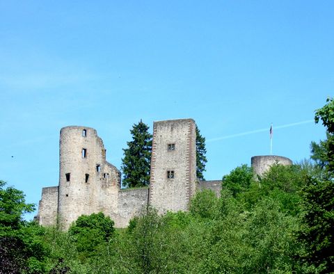 Eine alte Burg liegt auf einem Hügel, umgeben von üppigem Grün. Der Himmel ist blau und klar.