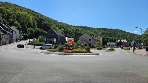 Ein Kreisverkehr umgeben von Häusern und grünen Hügeln. Der Himmel ist klar und blau, was eine ruhige Atmosphäre schafft.