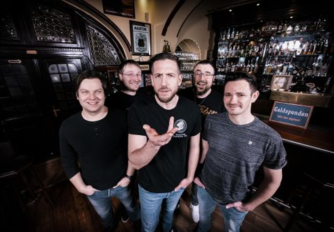 Un groupe se trouve dans un pub chaleureux.
Ils sourient et posent devant un bar avec de nombreuses boissons.