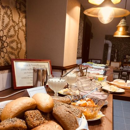 Ein Buffet mit verschiedenen Brötchen, Aufschnitt und frischen Früchten. Es gibt auch Desserts und eine ansprechende Präsentation.