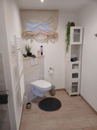 Ein modernes Badezimmer mit einer Dusche, einem WC und einem weißen Schrank. Der Boden ist aus Fliesen und der Raum ist hell und freundlich.