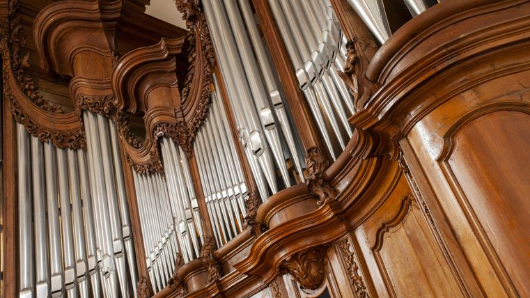 Eine beeindruckende Orgel mit kunstvollen Holzverzierungen und silbernen Pfeifen. Das Bild zeigt die Detailansicht des Instruments.