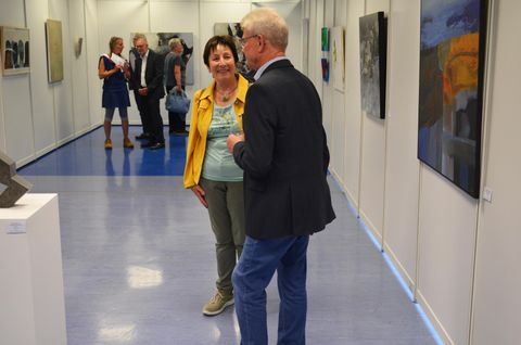 Eine Kunstausstellung mit mehreren Besuchern. Zwei Personen stehen im Vordergrund und unterhalten sich.