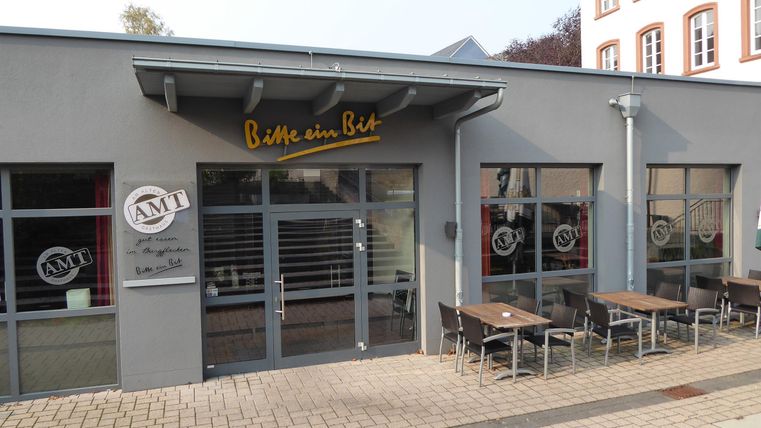 Ein modernes Restaurant mit großen Fenstern und einem einladenden Außenbereich. Tische stehen auf dem Bürgersteig, bereit für Gäste.