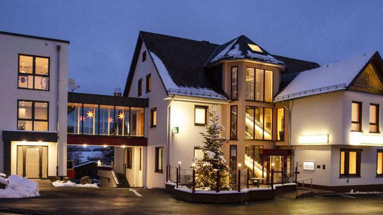 Ein modernes Gebäude in der Dämmerung, umgeben von Schnee. Die warmen Lichter der Fenster strahlen eine einladende Atmosphäre aus.