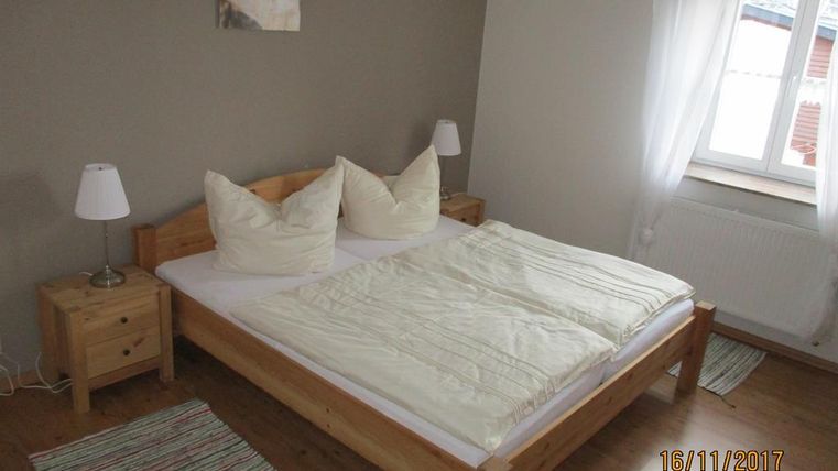 Ein gemütliches Schlafzimmer mit einem Doppelbett und zwei Kissen. Es gibt Nachttische mit Lampen und ein Fenster, das Tageslicht hereinlässt.