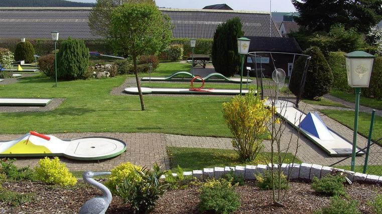 Ein Minigolfplatz mit grünem Rasen und verschiedenen Spielbahnen. Umgeben von Bäumen und Sträuchern, bietet die Anlage eine entspannte Atmosphäre.