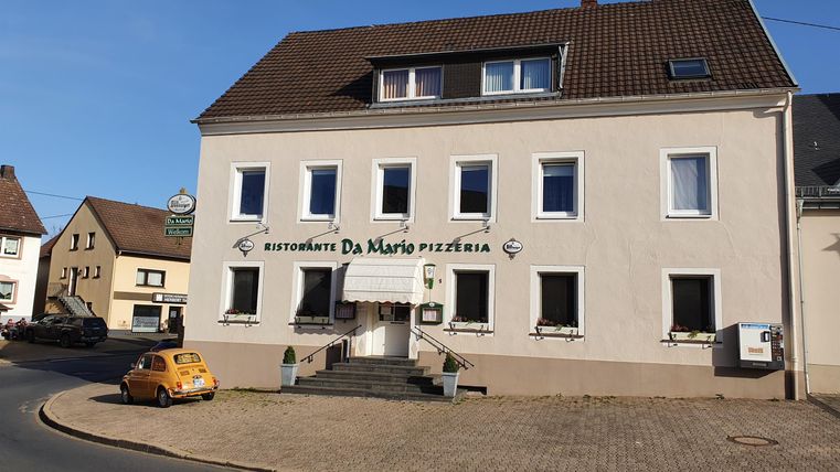 Ein Restaurantgebäude mit der Beschriftung „Da Mario“ an einer Straßenecke. Das Wetter ist sonnig und klar.