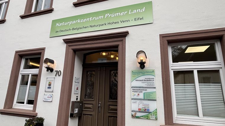 The image shows the nature park center Prümer Land with an inviting entrance area. Above the door is a sign with the name of the center and information about the nature parks in the region.